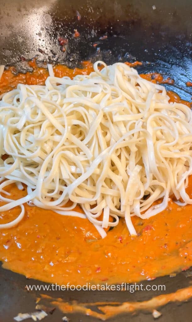 tossing cooked wheat noodles in creamy tomato coconut sauce