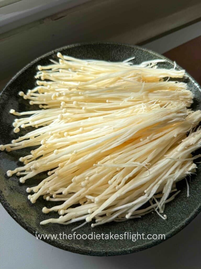 Separated enoki mushrooms arranged on a heat-proof plate before steaming