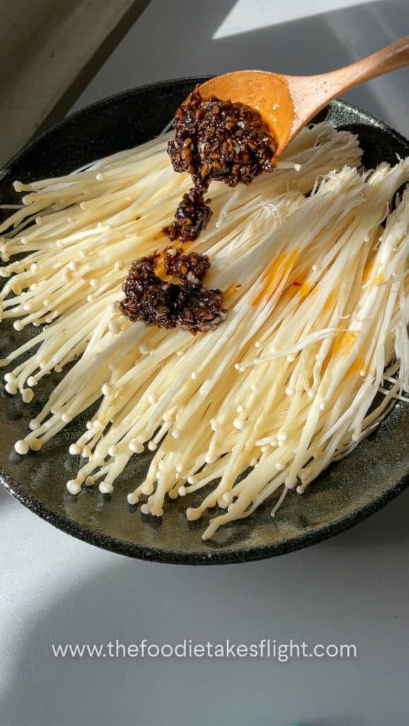 Pouring garlic chili sauce over fresh enoki mushrooms before steaming