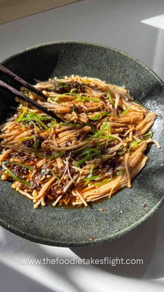 Plate of steamed enoki mushrooms topped with garlic, chili, green onions, and a drizzle of sesame oil.