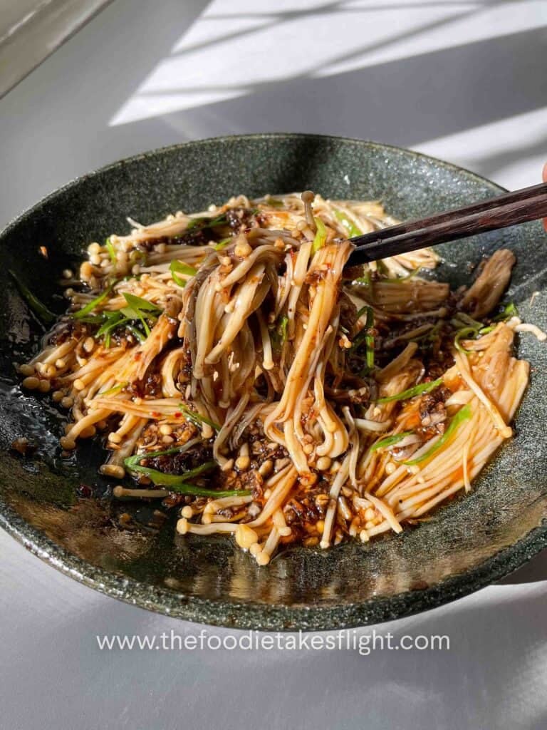 Plate of steamed enoki mushrooms topped with garlic, chili, green onions, and a drizzle of sesame oil.