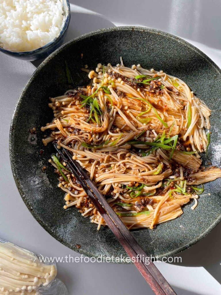 Plate of steamed enoki mushrooms topped with garlic, chili, green onions, and a drizzle of sesame oil.