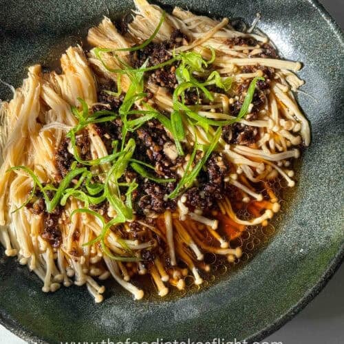 Plate of steamed enoki mushrooms topped with garlic, chili, green onions, and a drizzle of sesame oil.