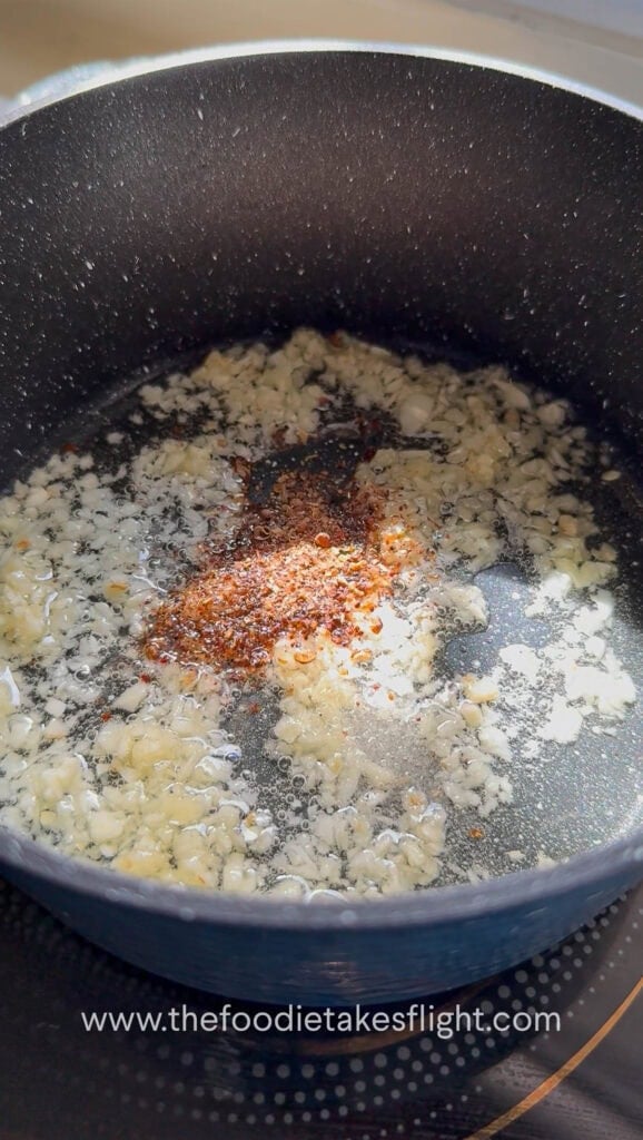 Garlic, chili powder, and Sichuan peppercorn sizzling in hot oil in a small pan