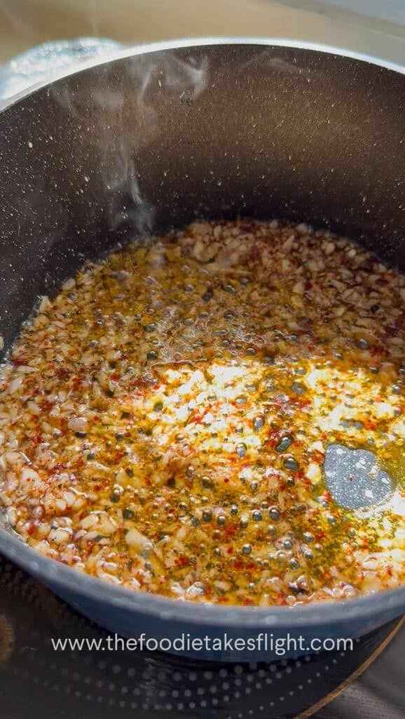 Garlic, chili powder, and Sichuan peppercorn sizzling in hot oil in a small pan