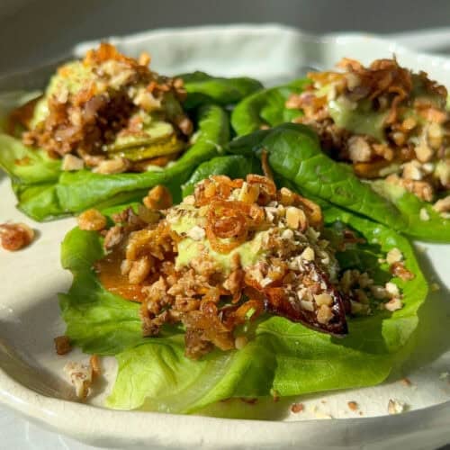 Close-up of a lettuce cup showing layers of squash, tofu, fried shallots, and chopped nuts