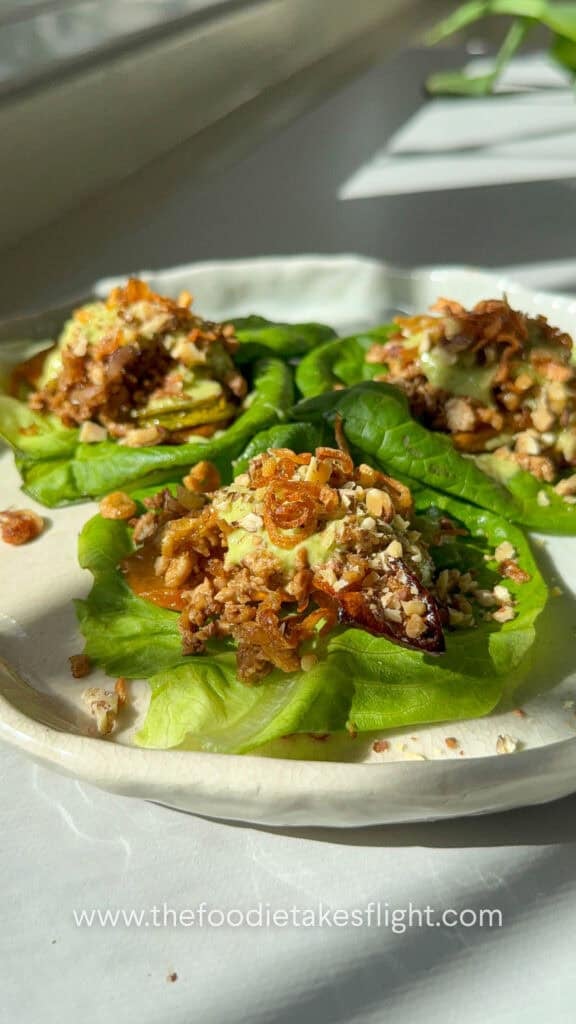 Close-up of a lettuce cup showing layers of squash, tofu, fried shallots, and chopped nuts