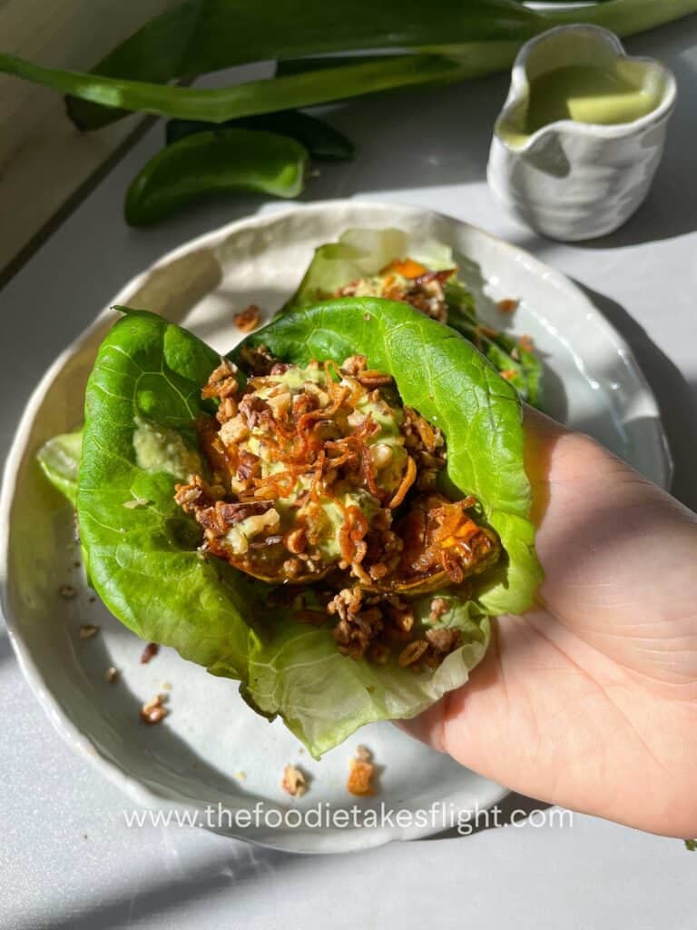 Close-up of a lettuce cup showing layers of squash, tofu, fried shallots, and chopped nuts