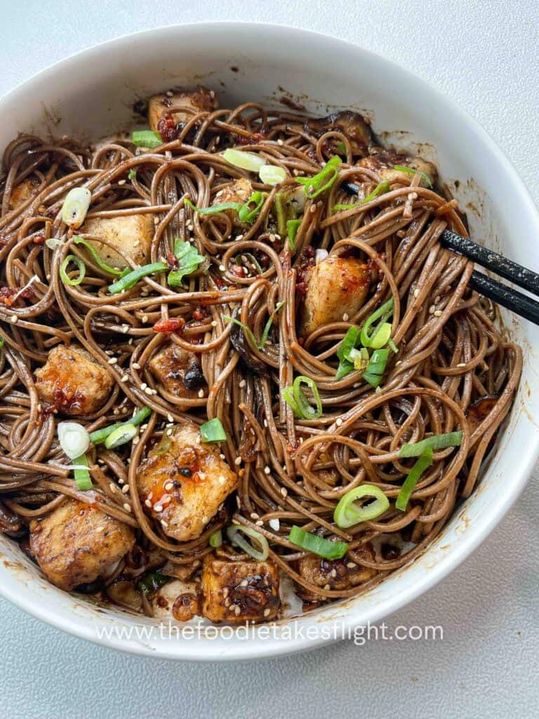 Bowl of soba noodles with black garlic miso dressing, topped with crispy tofu, mushrooms, and fried shallots.