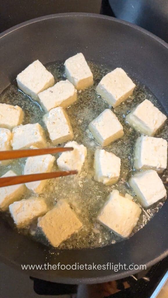 Tofu cubes sizzling in a skillet, turning golden and crisp