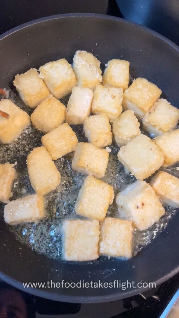 Tofu cubes sizzling in a skillet, turning golden and crisp