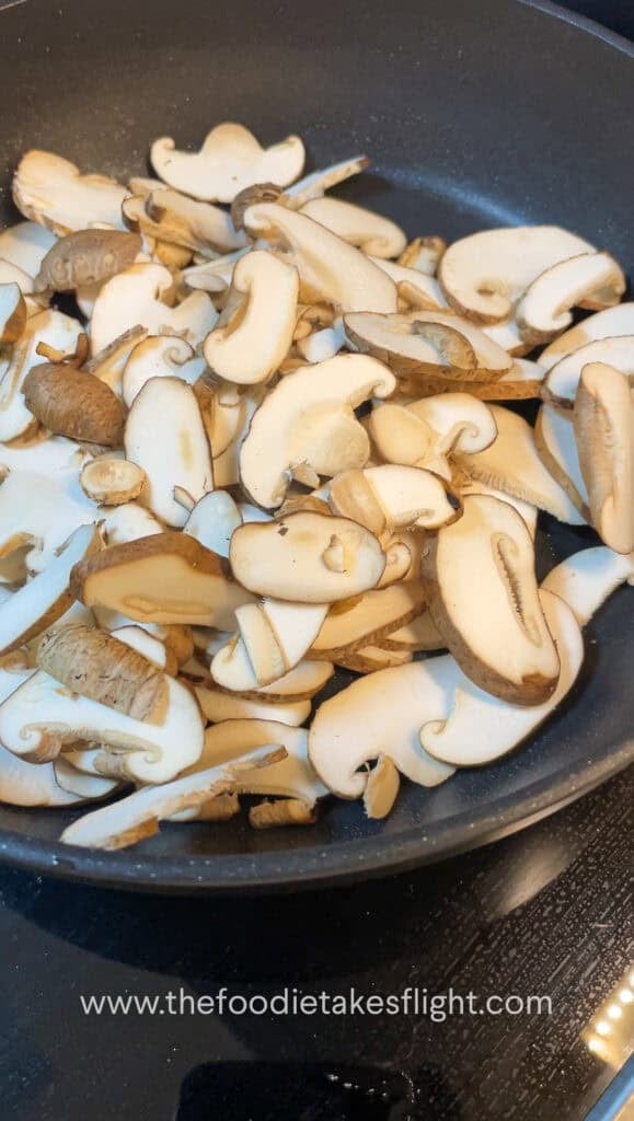 thinly sliced shiitake mushrooms cooking down in a pan