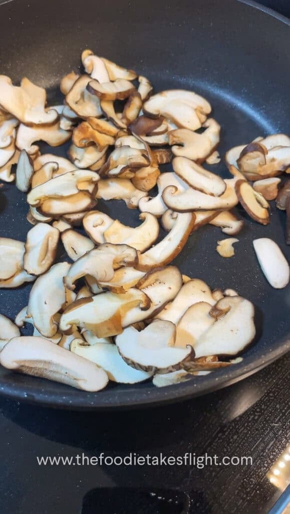 thinly sliced shiitake mushrooms cooking down in a pan