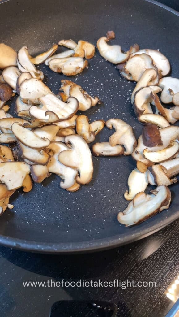 thinly sliced shiitake mushrooms cooking down in a pan