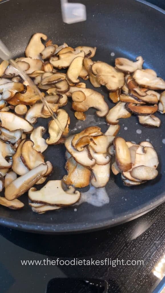 thinly sliced shiitake mushrooms cooking down in a pan