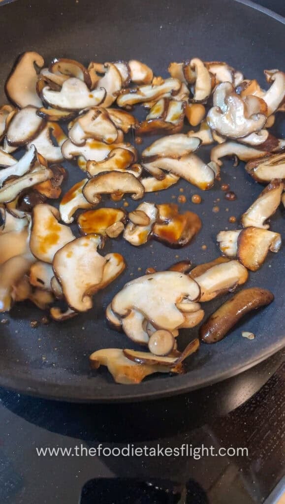 thinly sliced shiitake mushrooms cooking down in a pan