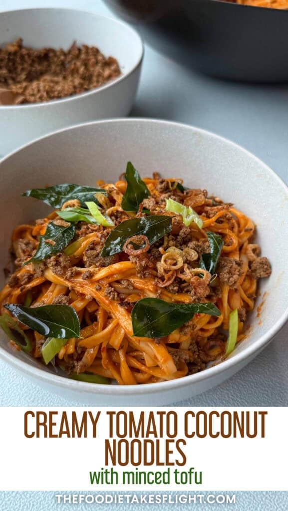 Close up of creamy tomato coconut noodles topped with fried curry leaves, crumbled tofu, and crispy shallots in a white bowl
