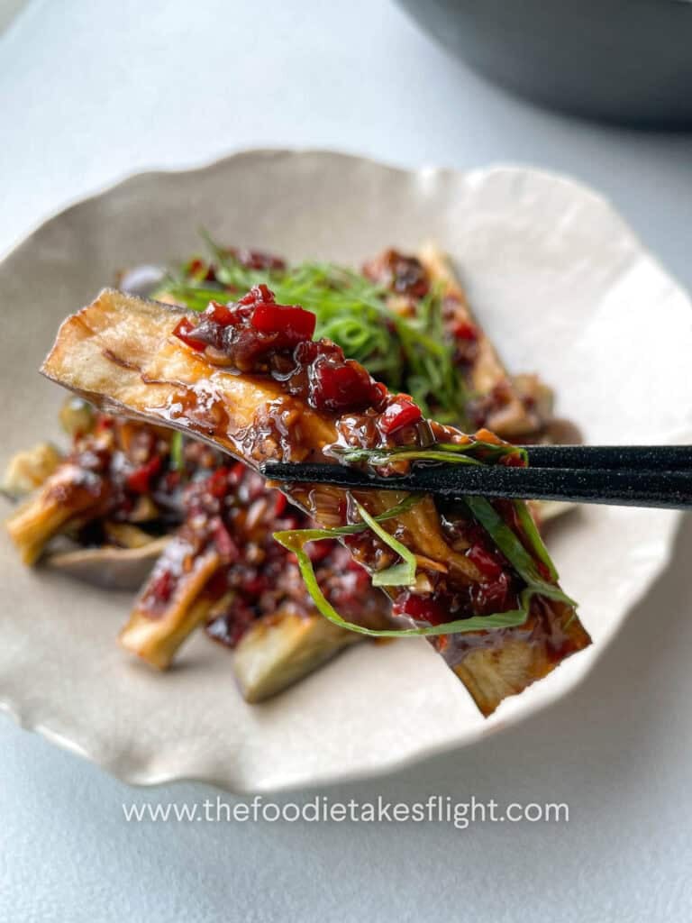 Close up of Chinese fried eggplant with spicy garlic sauce, with small red bell pepper pieces and thinly sliced green onions