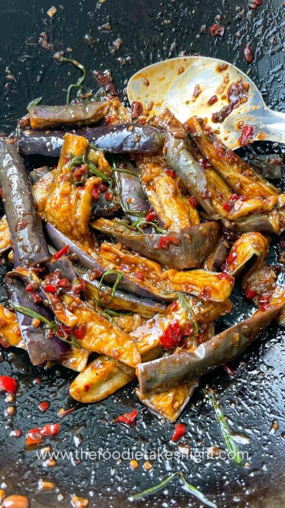 Tossing fried eggplant in sauce with red bell peppers and chili in a wok