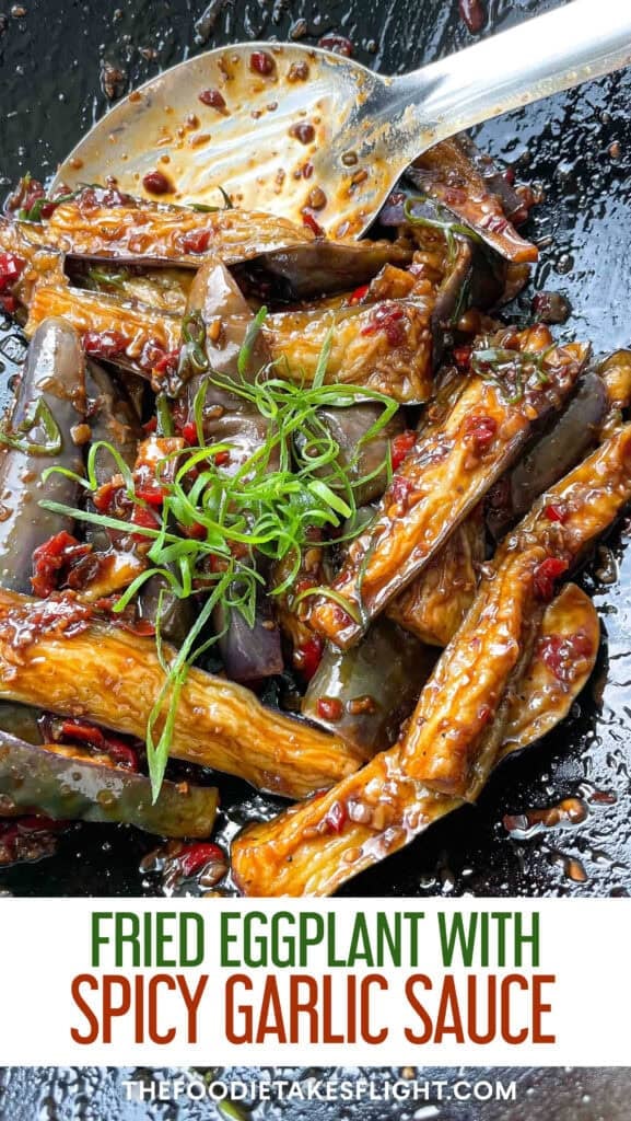 Bowl of Chinese fried eggplant with spicy garlic sauce, with small red bell pepper pieces and thinly sliced green onions