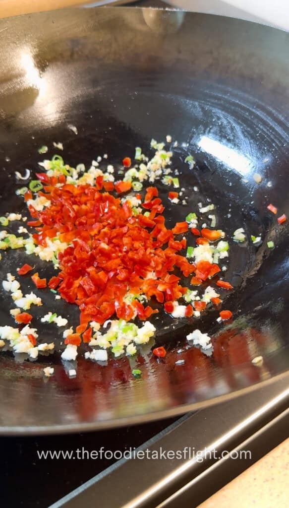 Diced bell pepper and aromatics stir frying in oil in a wok