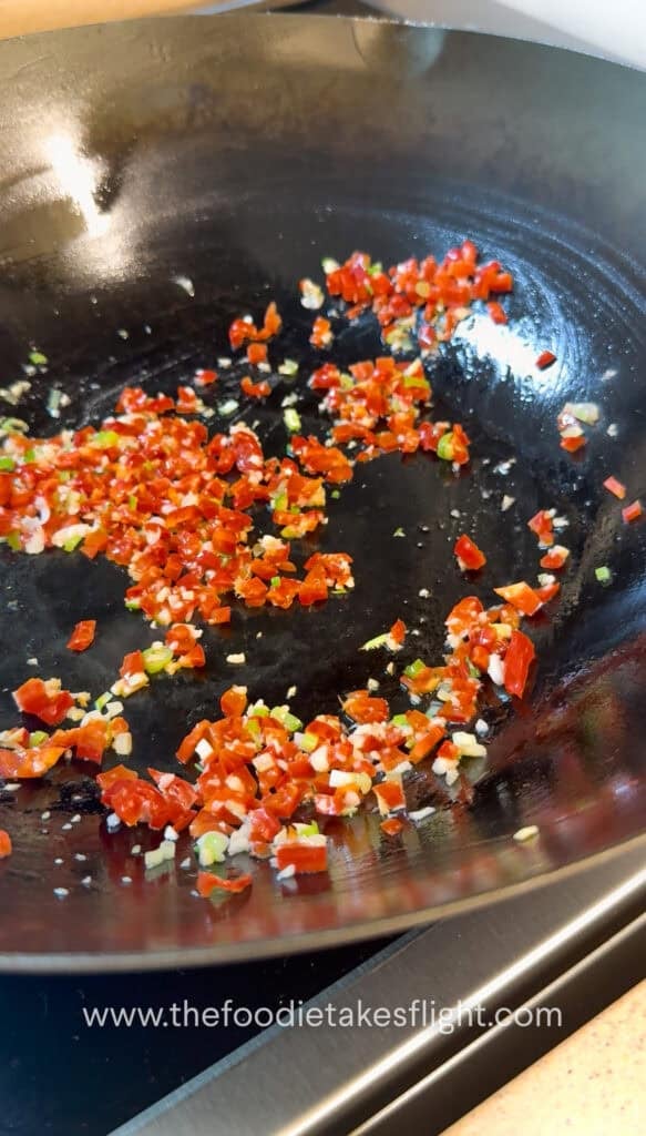 Diced bell pepper and aromatics stir frying in oil in a wok