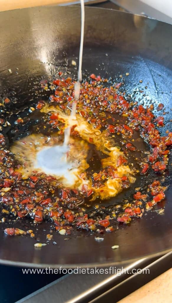 Pouring corn starch slurry into a wok of spicy garlic sauce