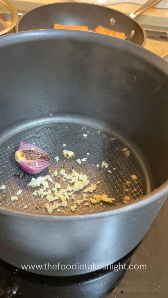 Red onion halves charring in a soup pot with minced garlic