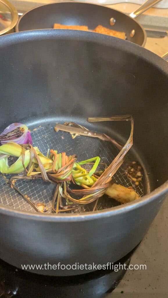 Red onion halves charring in a soup pot with minced garlic and lemongrass stalk