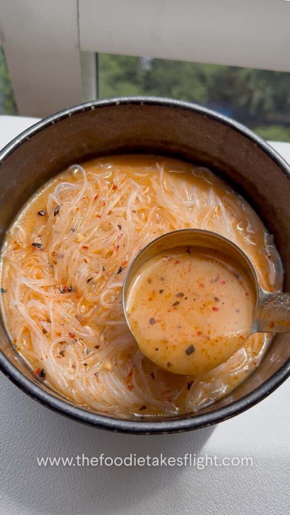 Adding spicy lemongrass coconut soup to a bowl of vermicelli noodles
