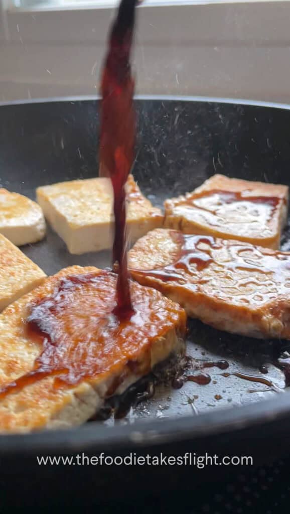 Pouring sauce over pan fried tofu in a skillet