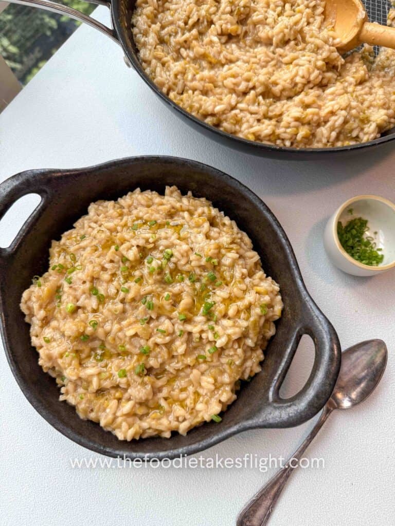 Bowl of caramelised leeks risotto topped with chives, olive oil drizzle, and vegan parmesan