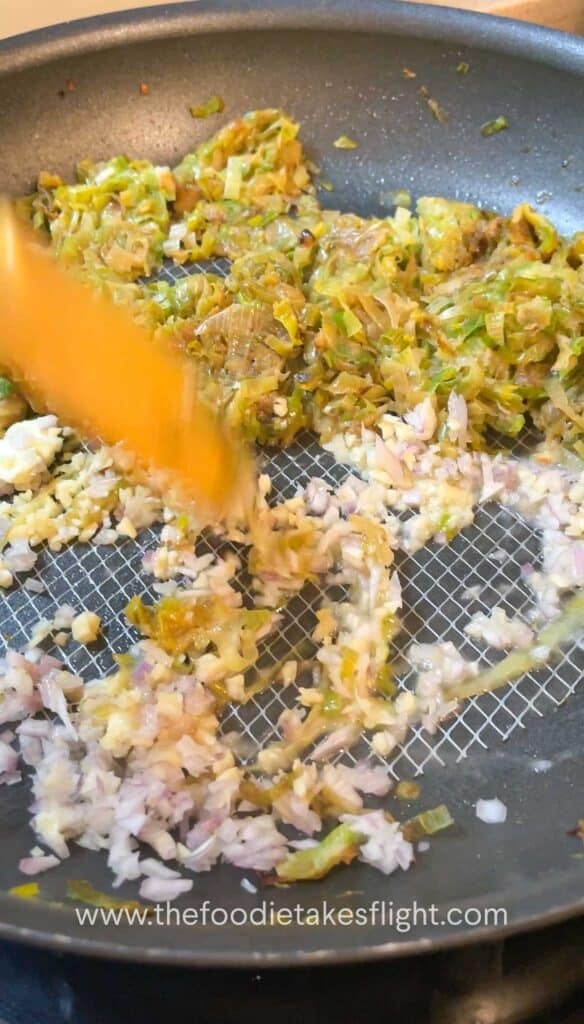 Caramelised leeks pushed to the side of the pan with shallots and garlic sautéing beside them