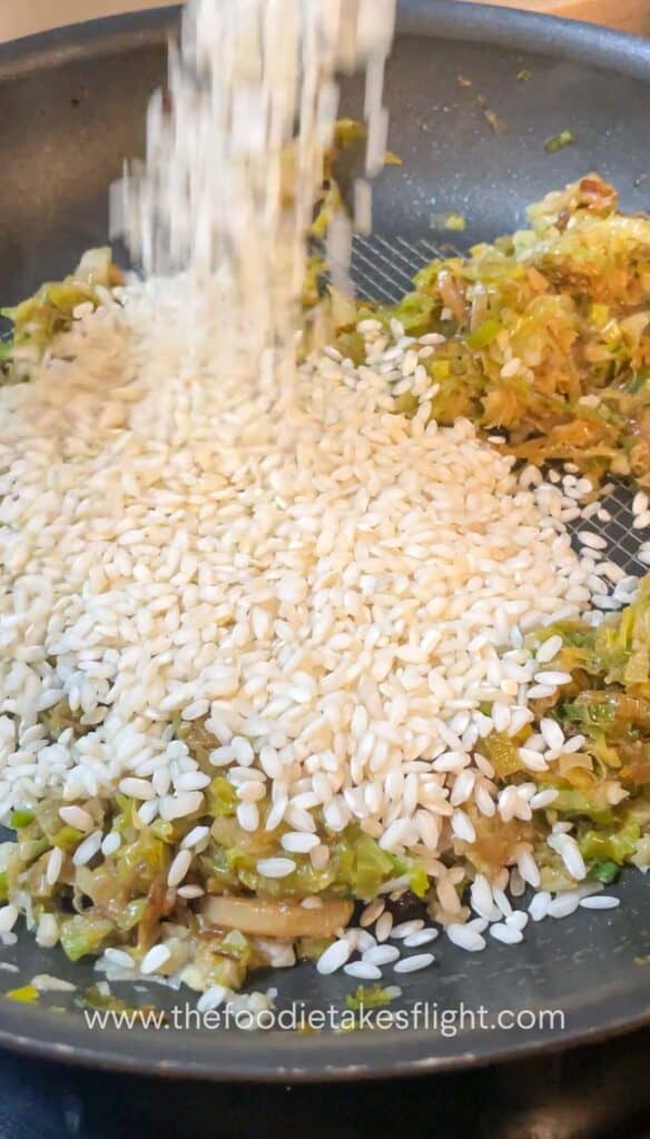 Arborio rice being stirred into the leeks mixture until glossy and lightly toasted
