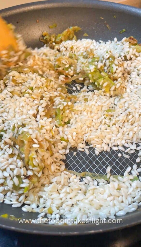 Arborio rice being stirred into the leeks mixture until glossy and lightly toasted