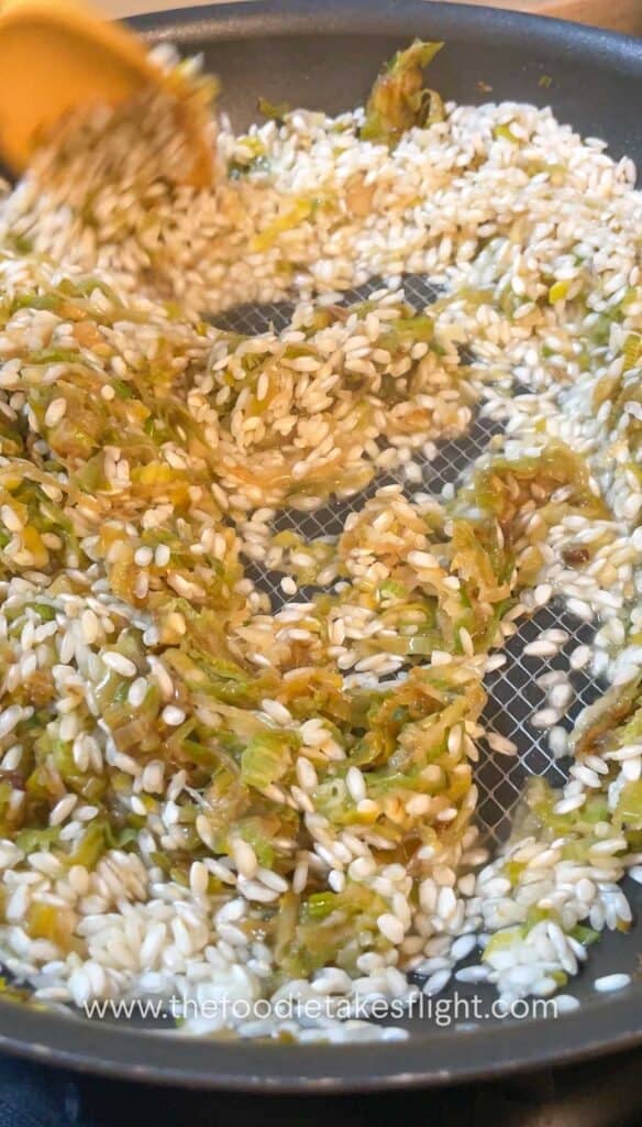 Arborio rice being stirred into the leeks mixture until glossy and lightly toasted