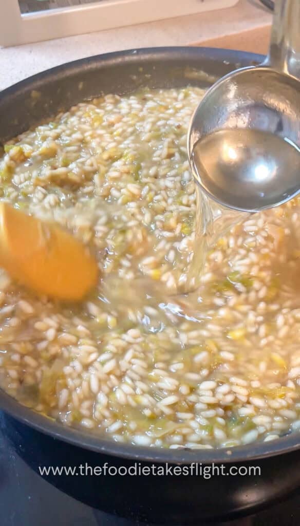 adding more broth to grains of arborio rice slowly cooking down in a pan
