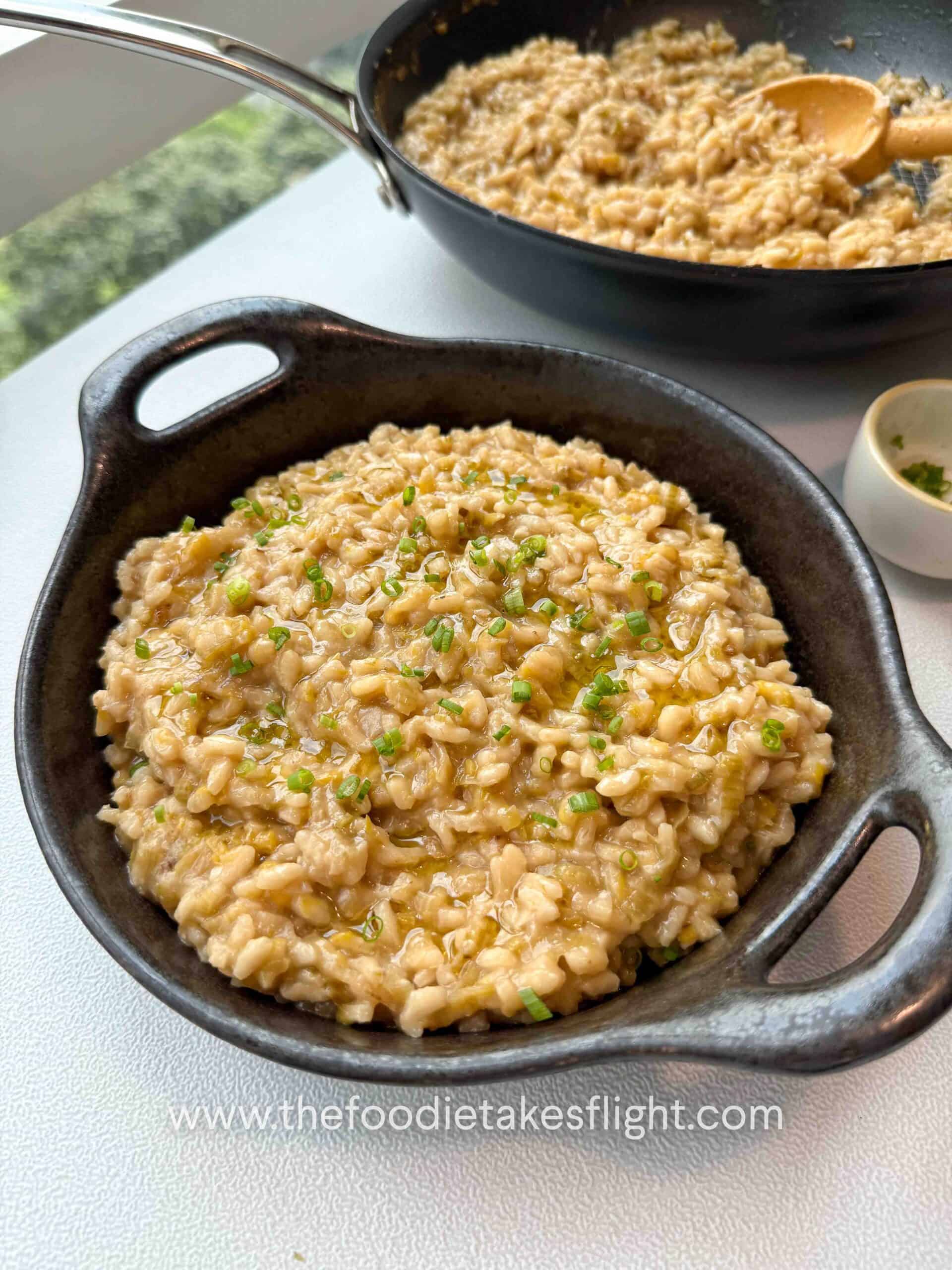 Bowl of caramelised leeks risotto topped with chives, olive oil drizzle, and vegan parmesan
