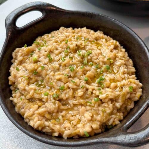 Bowl of caramelised leeks risotto topped with chives, olive oil drizzle, and vegan parmesan