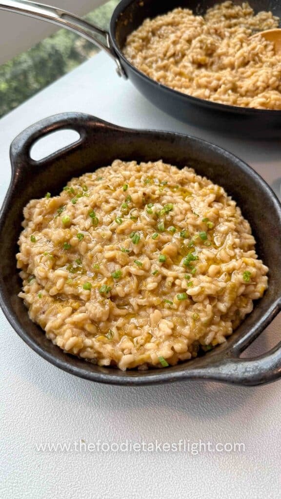 Bowl of caramelised leeks risotto topped with chives, olive oil drizzle, and vegan parmesan