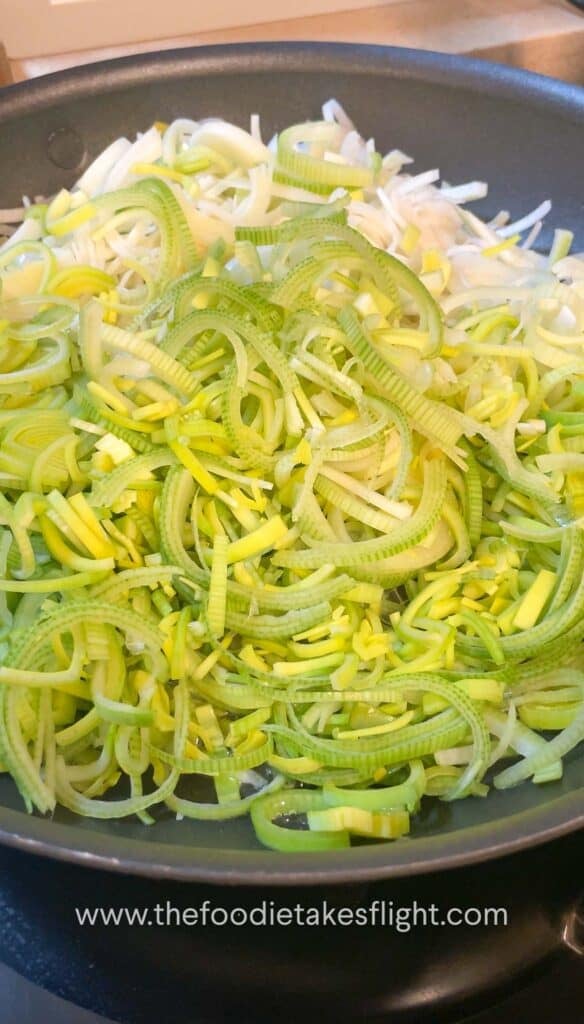 Thinly sliced leeks cooking in a pan until soft and golden brown.