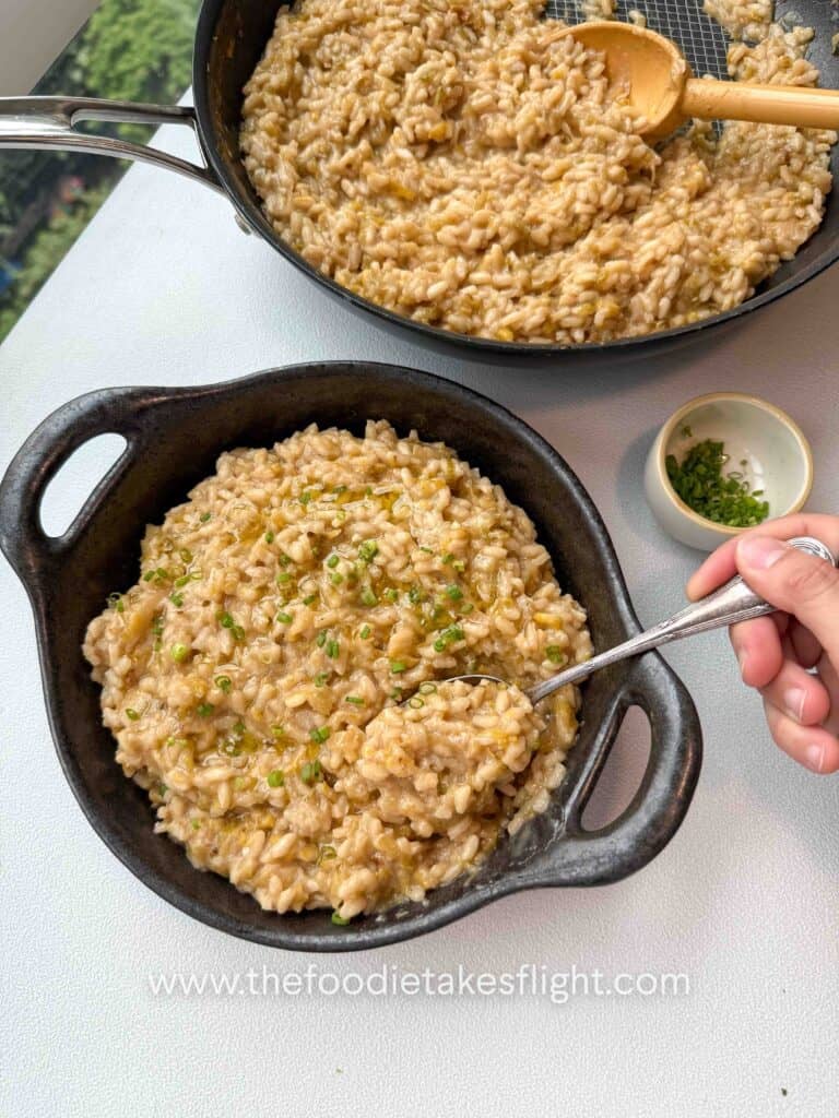 Bowl of caramelised leeks risotto topped with chives, olive oil drizzle, and vegan parmesan