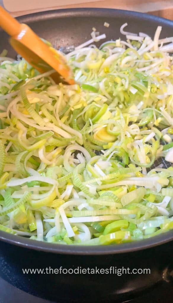 Thinly sliced leeks cooking in a pan until soft and golden brown.