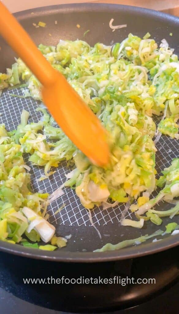 Thinly sliced leeks cooking in a pan until soft and golden brown.
