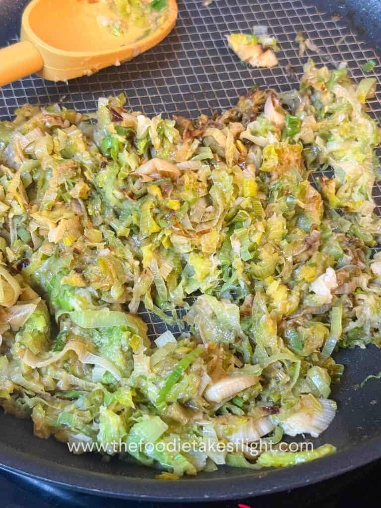 Thinly sliced leeks cooking in a pan until soft and golden brown.