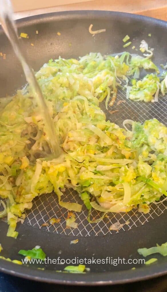 Thinly sliced leeks cooking in a pan until soft and golden brown.