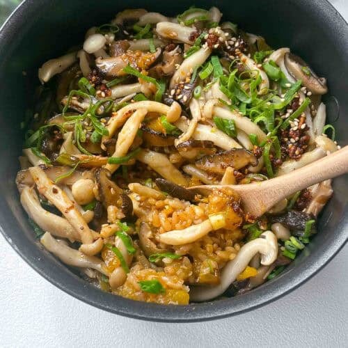 a pot with cooked pumpkin and mushroom rice topped with sliced green scallions and chili oil
