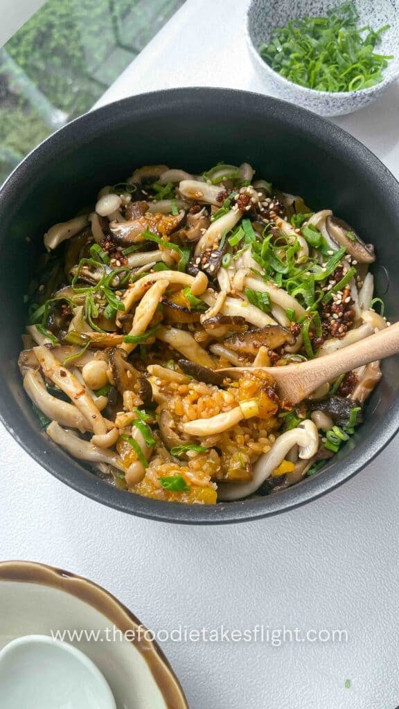 a pot with cooked pumpkin and mushroom rice topped with sliced green scallions and chili oil