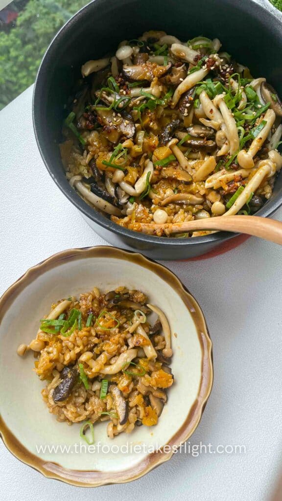 a pot and bowl filled with cooked pumpkin and mushroom short grain rice topped with sliced green scallions and chili oil