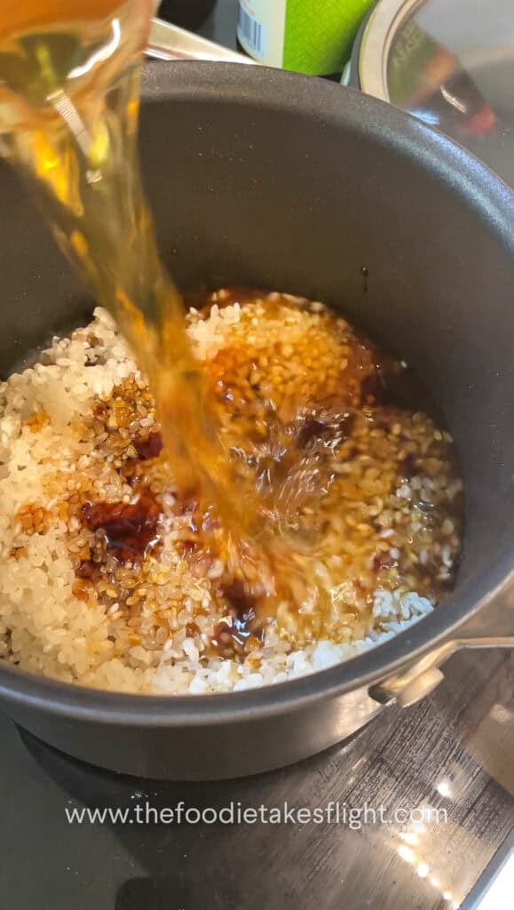 Rice, soy sauce, and mushroom broth being stirred together in a pot